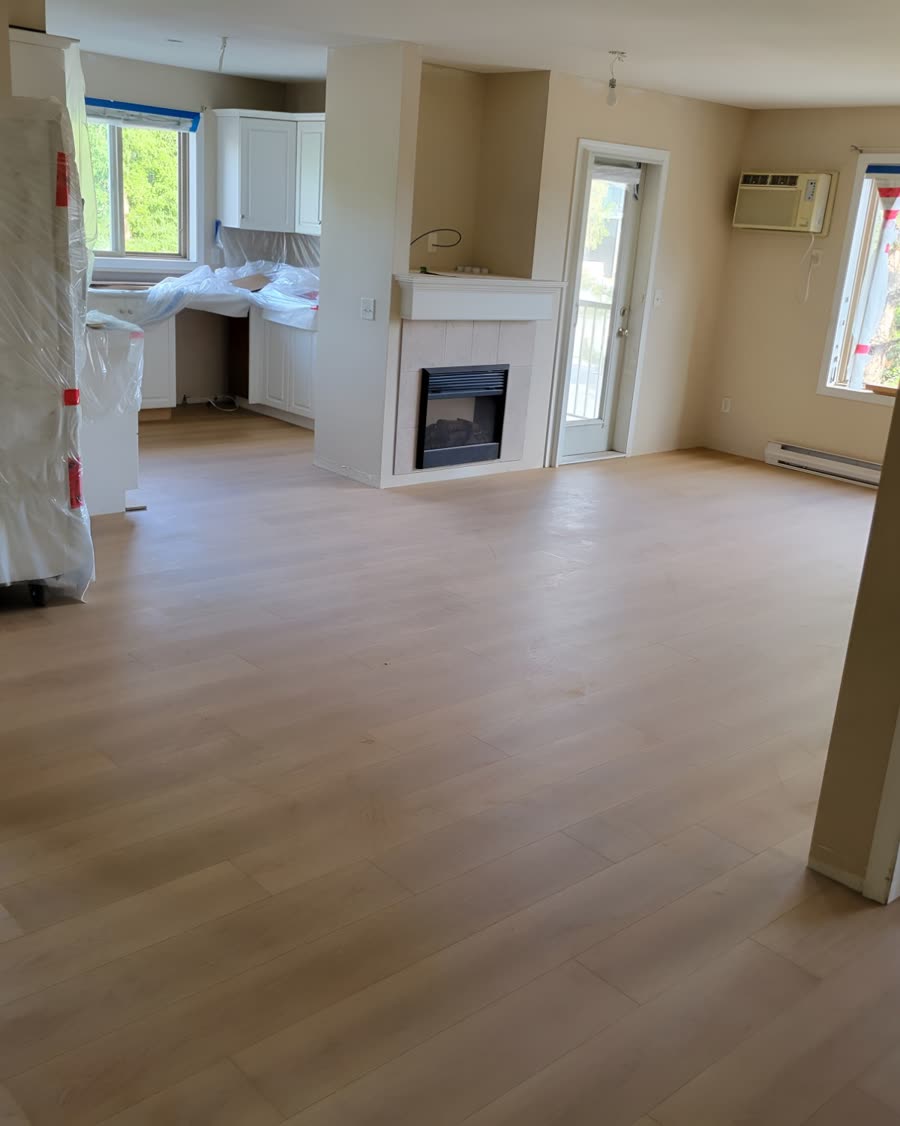 Wide plank laminate flooring laid through an open plan living room and kitchen during a renovation.