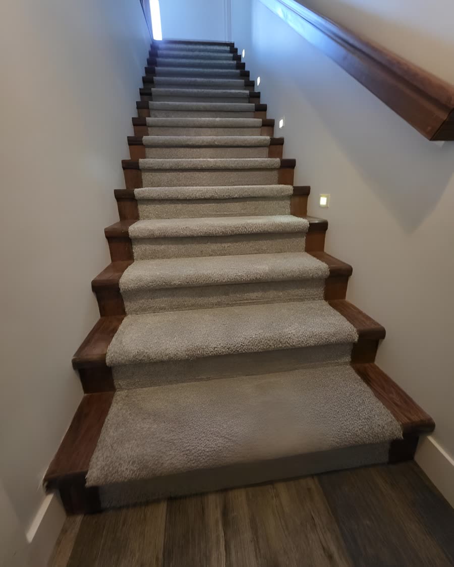 Carpet fitted to a staircase with stained wood nosings and lit step lights.