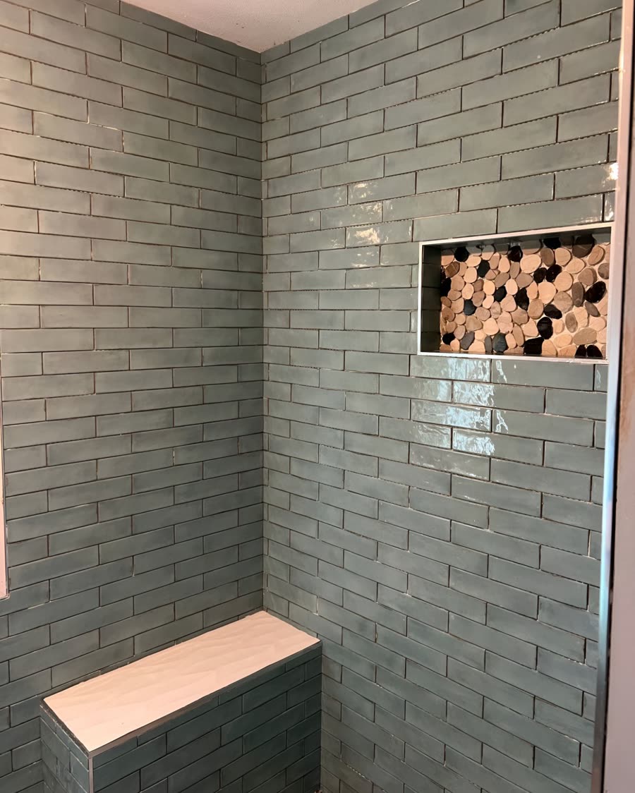A shower tiled in green subway tile with a built in bench and a pebble mosaic niche.